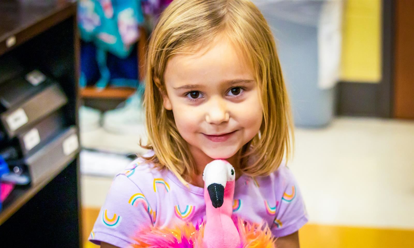 A girl smiles while holding a flamingo toy